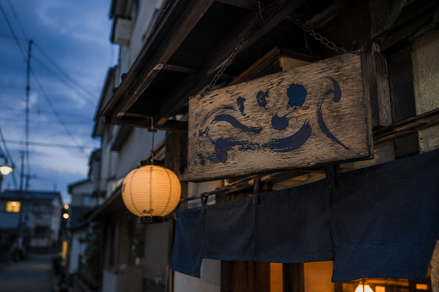 店の入口に下がる木の看板と藍の暖簾、提灯の灯り